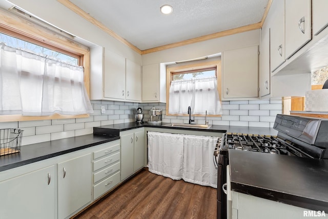 kitchen with dark wood-style flooring, a sink, gas stove, decorative backsplash, and dark countertops