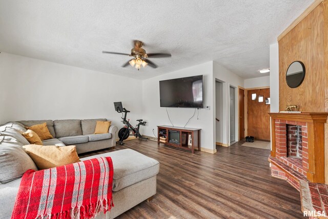 living area with baseboards, dark wood-style floors, ceiling fan, a textured ceiling, and a brick fireplace