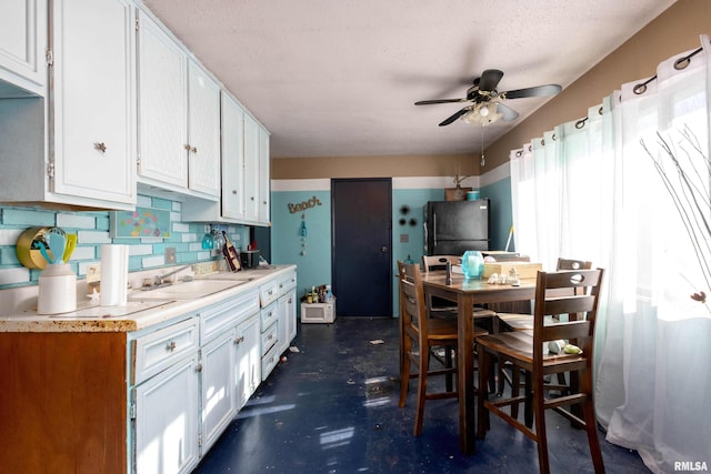 kitchen featuring tasteful backsplash, white cabinetry, sink, black fridge, and a textured ceiling