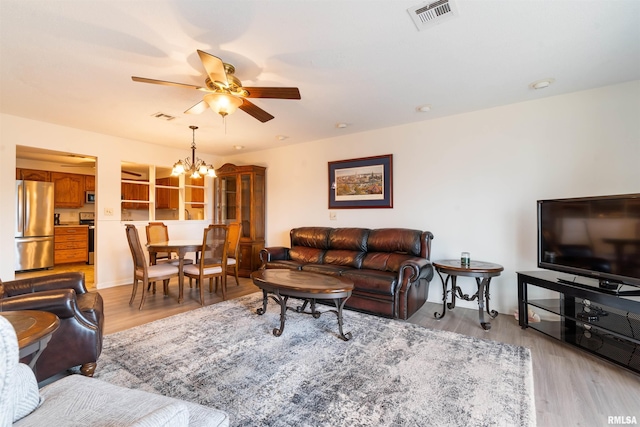 living room with ceiling fan with notable chandelier and light hardwood / wood-style flooring