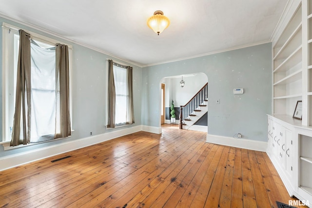 spare room with crown molding, built in features, and light hardwood / wood-style flooring