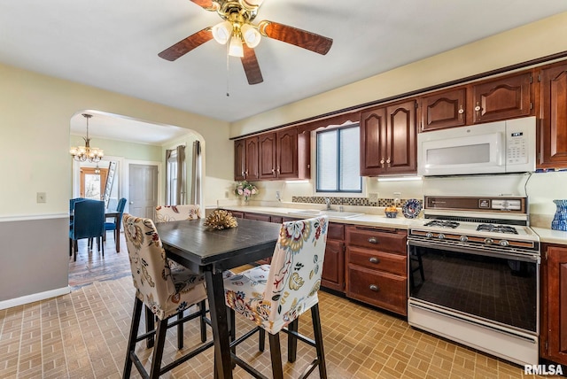 kitchen with hanging light fixtures, white appliances, ceiling fan with notable chandelier, and sink