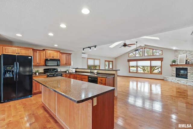 kitchen featuring sink, black appliances, a stone fireplace, kitchen peninsula, and light wood-type flooring