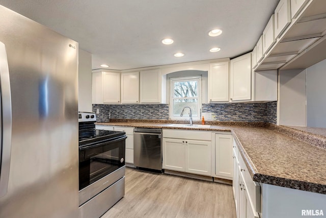 kitchen with appliances with stainless steel finishes, white cabinets, a sink, and light wood finished floors