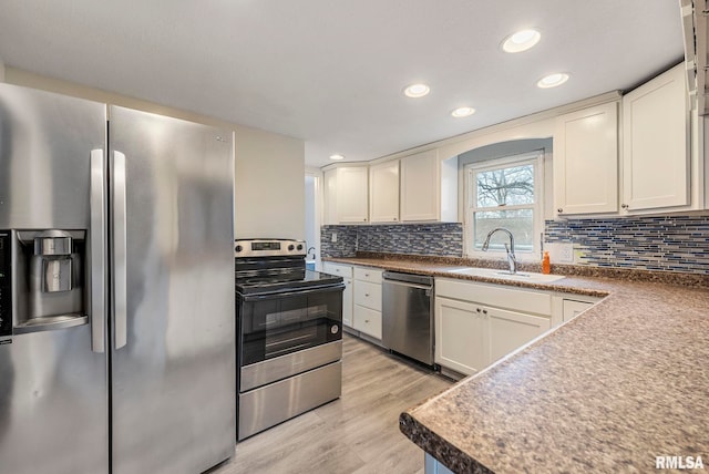 kitchen with stainless steel appliances, tasteful backsplash, light wood-style floors, white cabinetry, and a sink