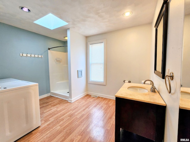 bathroom with a skylight, vanity, wood-type flooring, a shower, and washer / dryer