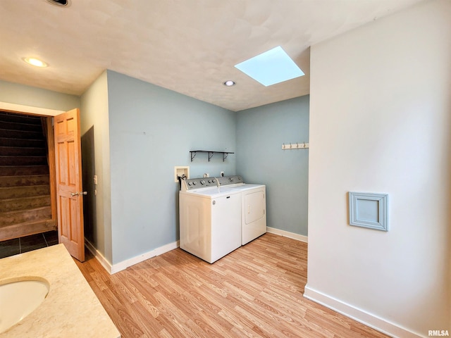 washroom with a skylight, washer and clothes dryer, light hardwood / wood-style floors, and sink