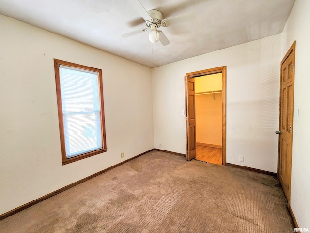 unfurnished bedroom with a spacious closet, light colored carpet, ceiling fan, and a closet