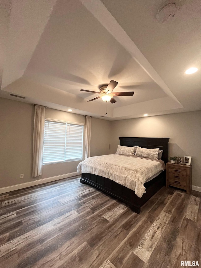 bedroom featuring ceiling fan, dark hardwood / wood-style flooring, and a tray ceiling