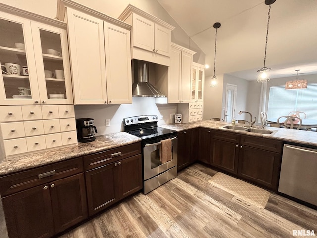 kitchen with lofted ceiling, sink, pendant lighting, stainless steel appliances, and wall chimney range hood