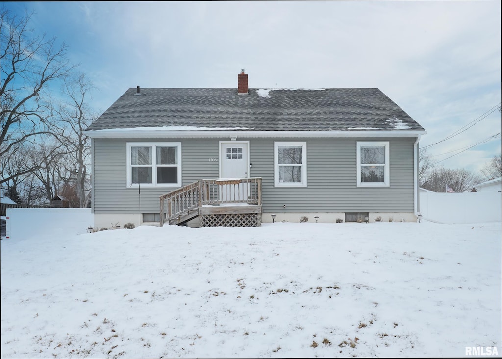 snow covered rear of property featuring a shingled roof and a chimney