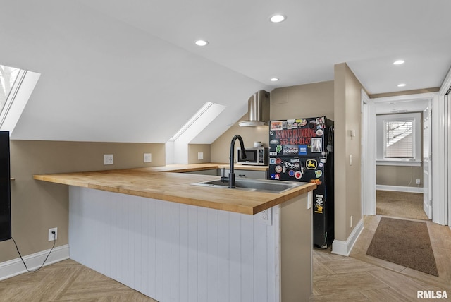 kitchen with butcher block countertops, light parquet floors, kitchen peninsula, and wall chimney exhaust hood