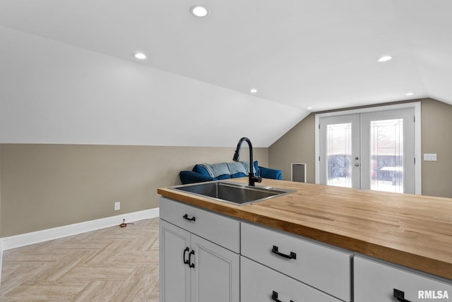 kitchen with sink, wooden counters, white cabinets, vaulted ceiling, and light parquet flooring