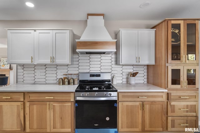 kitchen featuring premium range hood, stainless steel gas range, decorative backsplash, and white cabinets