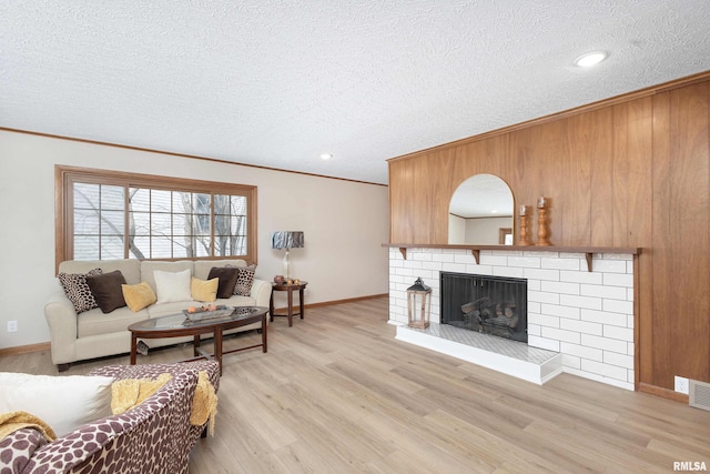 living room featuring light wood-type flooring, a brick fireplace, wood walls, ornamental molding, and a textured ceiling