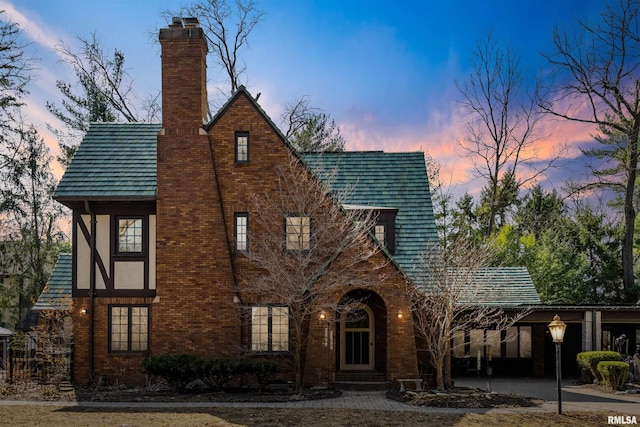 tudor home with entry steps, a chimney, and brick siding