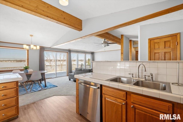 kitchen with lofted ceiling with beams, tile counters, stainless steel dishwasher, backsplash, and sink