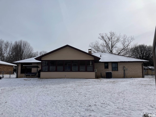 snow covered house with central AC unit and a sunroom