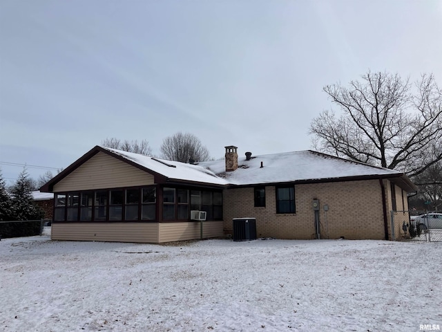 snow covered back of property with cooling unit and a sunroom