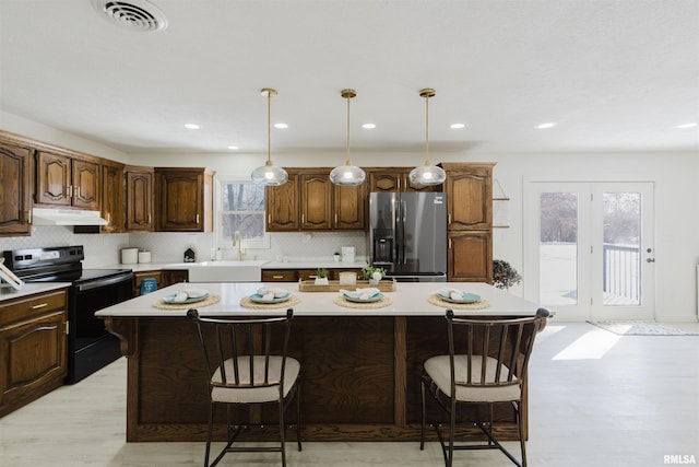 kitchen featuring a kitchen island, a sink, stainless steel fridge, black range with electric cooktop, and under cabinet range hood