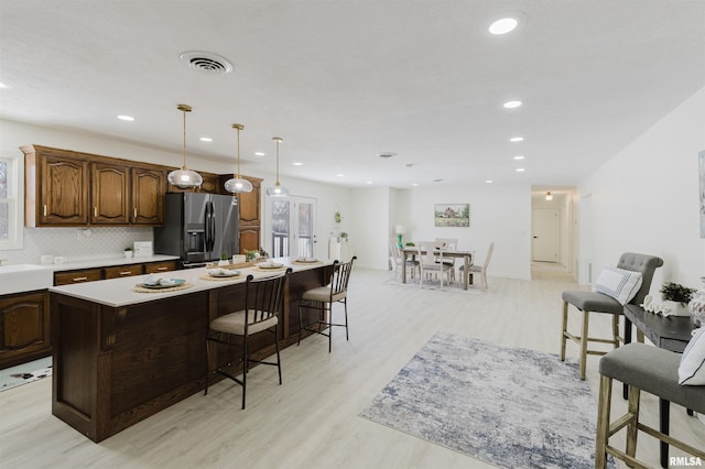 kitchen featuring a kitchen island, light wood-style floors, light countertops, hanging light fixtures, and stainless steel fridge