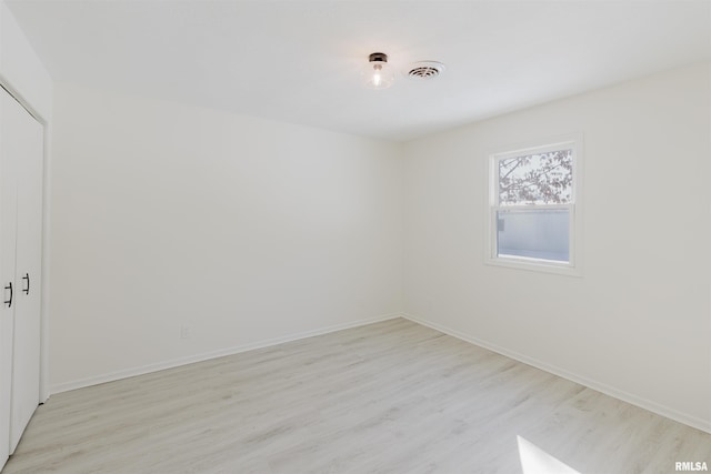 spare room featuring light wood-style floors, visible vents, and baseboards