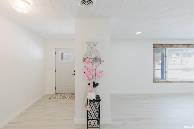 foyer with light wood-type flooring, visible vents, a textured ceiling, and baseboards