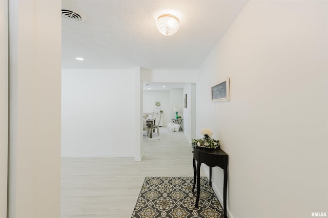 hall featuring light wood-style floors, visible vents, a textured ceiling, and baseboards