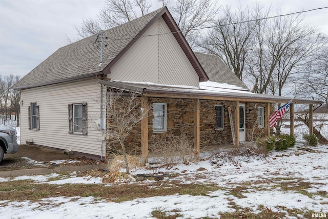 view of snowy exterior with a shingled roof and stone siding