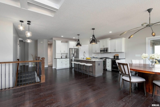 kitchen with white cabinets, decorative backsplash, dark wood-type flooring, stainless steel appliances, and a kitchen bar