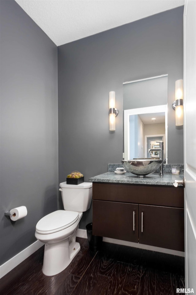 half bathroom with wood finished floors, vanity, toilet, and baseboards