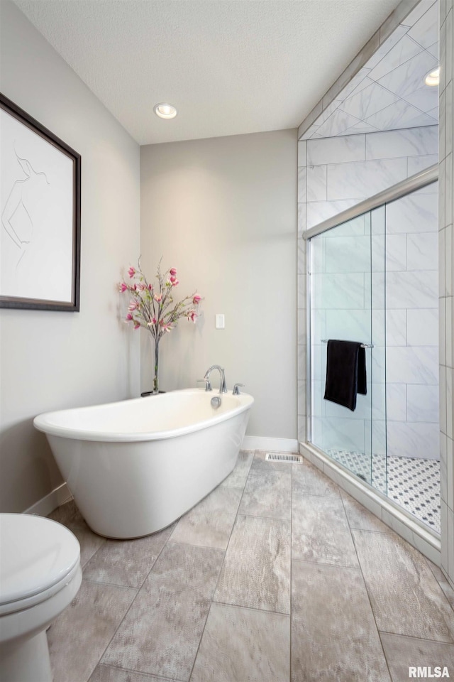 bathroom featuring a textured ceiling, a freestanding tub, a shower stall, and toilet