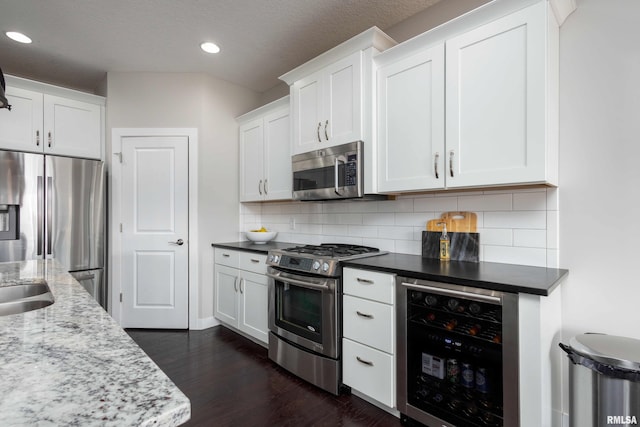 kitchen with appliances with stainless steel finishes, wine cooler, white cabinets, and tasteful backsplash