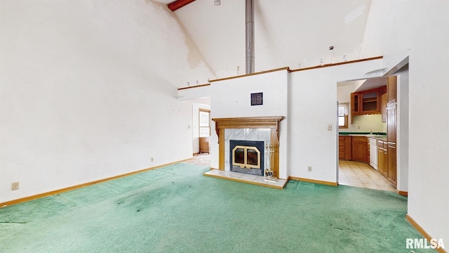 unfurnished living room featuring light carpet, a tiled fireplace, a towering ceiling, and baseboards