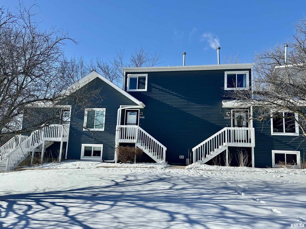 snow covered rear of property featuring stairs