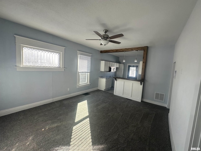 unfurnished living room featuring a textured ceiling, dark carpet, visible vents, and baseboards