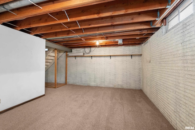 below grade area featuring carpet flooring, brick wall, and stairs