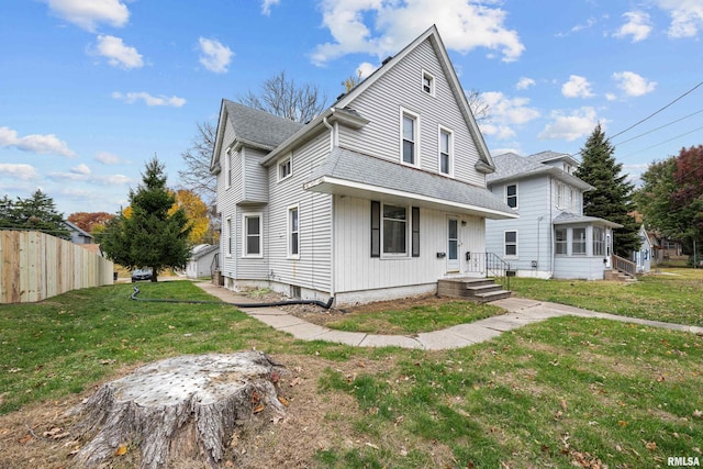 traditional-style home with a front yard, roof with shingles, and fence