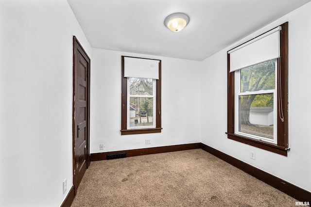 spare room featuring carpet floors, plenty of natural light, visible vents, and baseboards