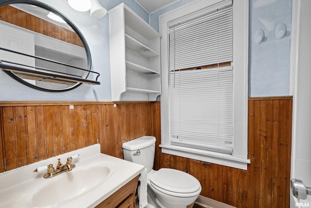 bathroom featuring toilet, wooden walls, and vanity