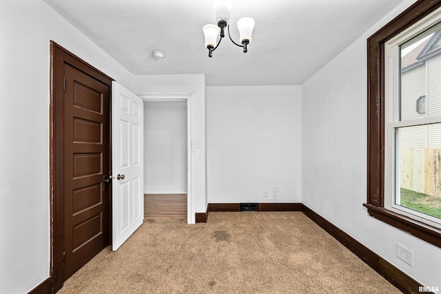empty room with an inviting chandelier, carpet, visible vents, and baseboards
