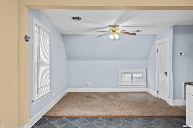 additional living space with dark colored carpet, visible vents, vaulted ceiling, and ceiling fan