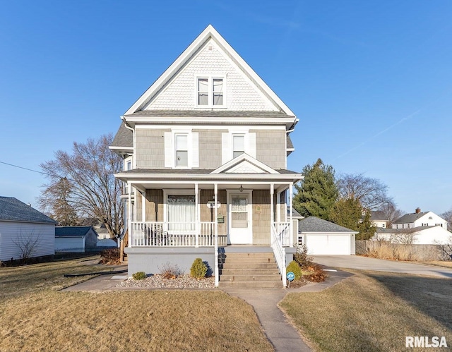 view of front of property with covered porch, a detached garage, and a front yard