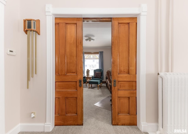 corridor featuring baseboards, radiator heating unit, and light colored carpet