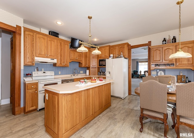 kitchen with under cabinet range hood, white appliances, a center island, decorative light fixtures, and light countertops