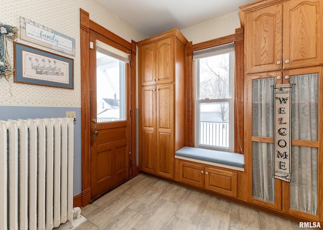 doorway to outside with wallpapered walls, radiator, and plenty of natural light