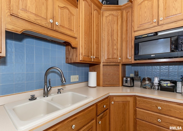 kitchen featuring black microwave, a sink, decorative backsplash, and light countertops