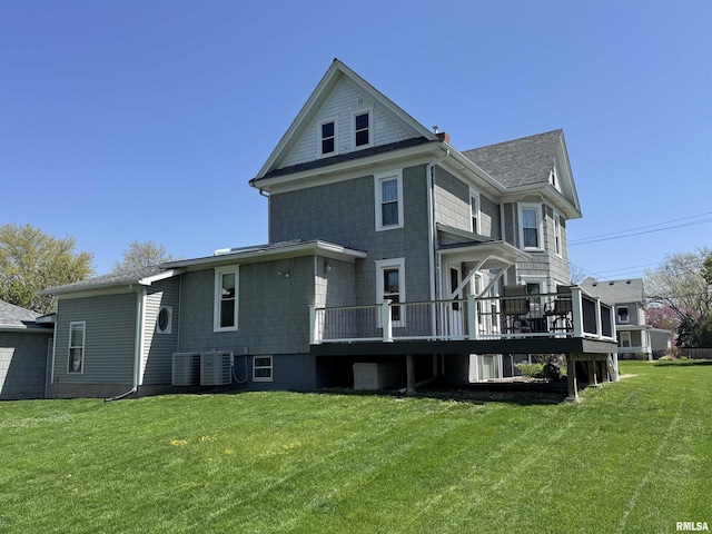 back of property with a deck, roof with shingles, central AC, and a lawn