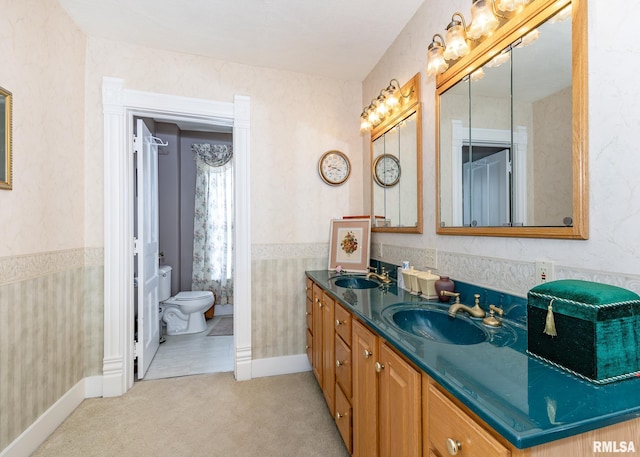 bathroom with toilet, double vanity, a sink, and wallpapered walls