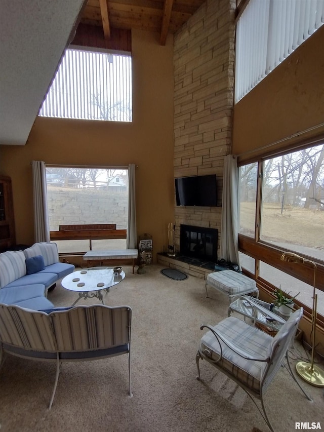 carpeted living area with beam ceiling, a healthy amount of sunlight, a stone fireplace, and a high ceiling